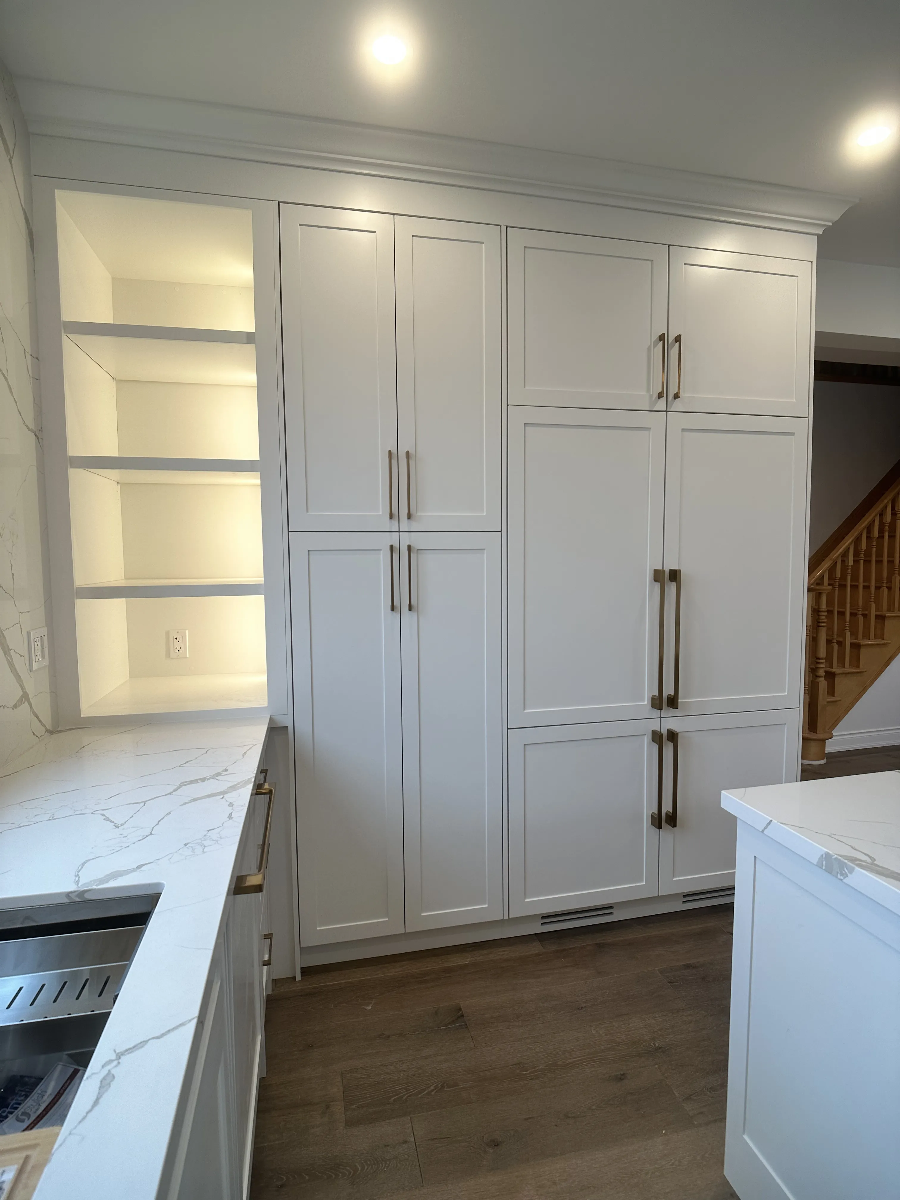 A tall run of custom cabinetry in soft white with brass hardware, built to the opening rather than bought to a standard size