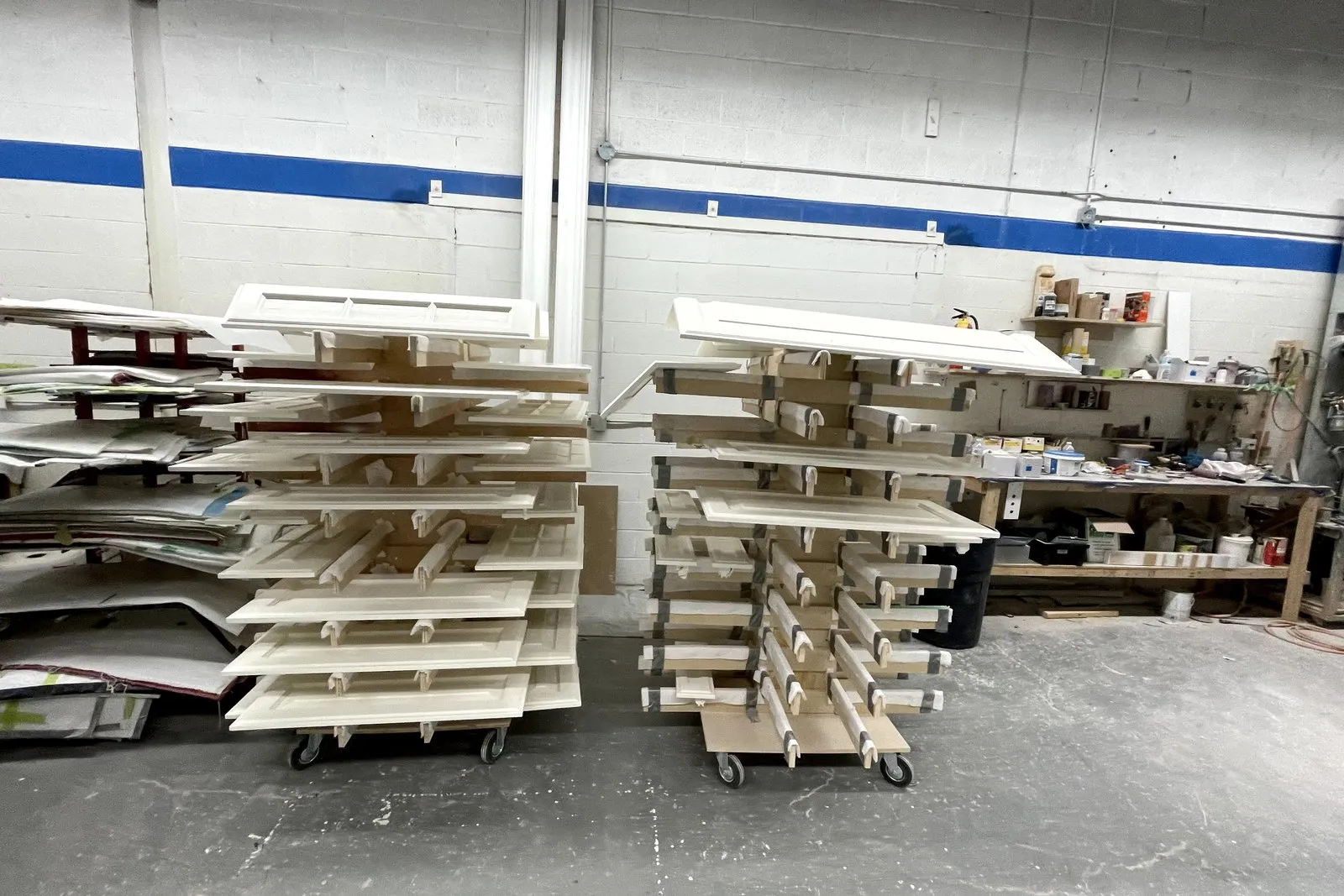 Racks of sprayed doors and drawer fronts filling the shop floor, each set built for one kitchen