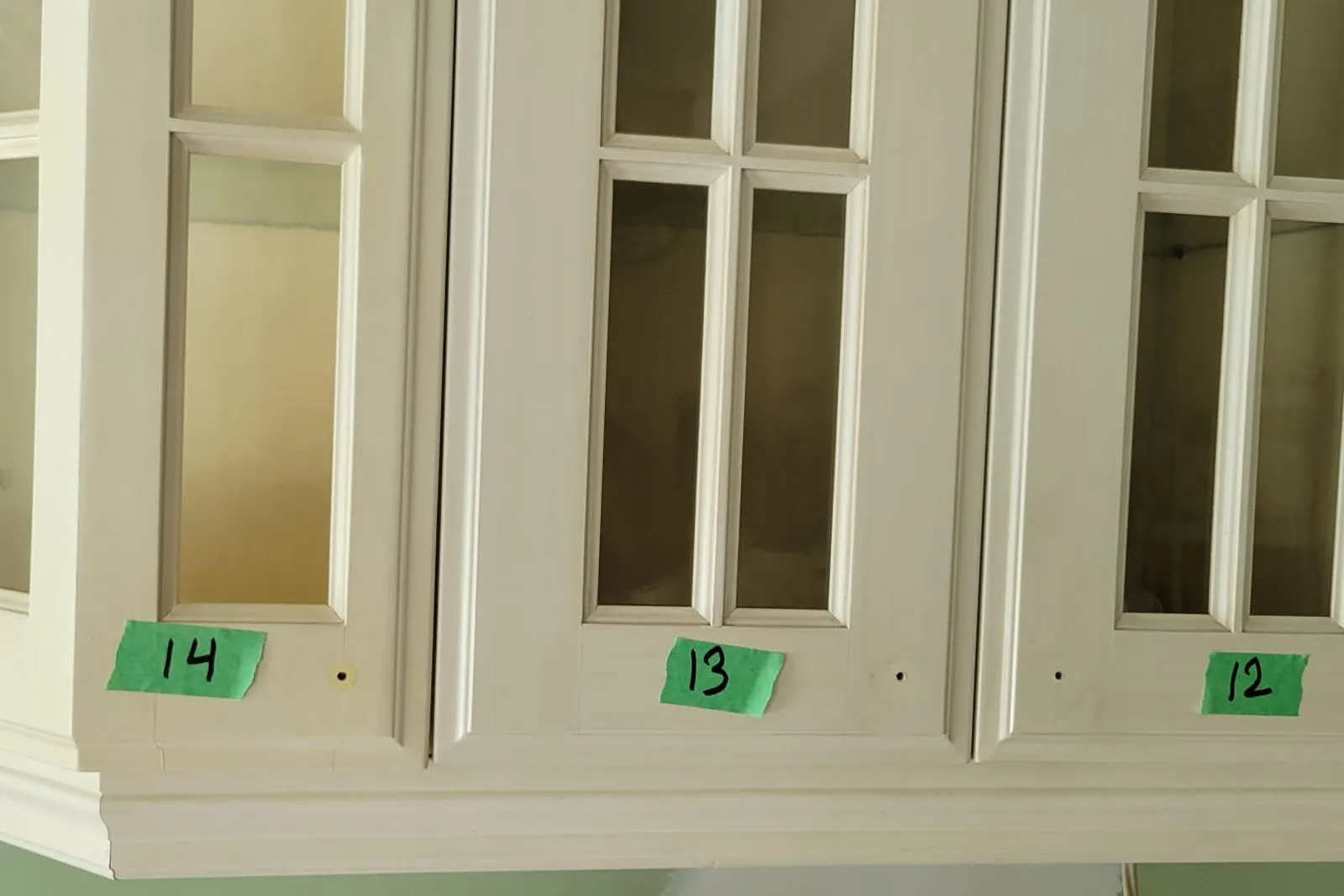 Crown moulding and mullioned glass doors fitted to a cabinet run, each opening numbered on green tape during installation