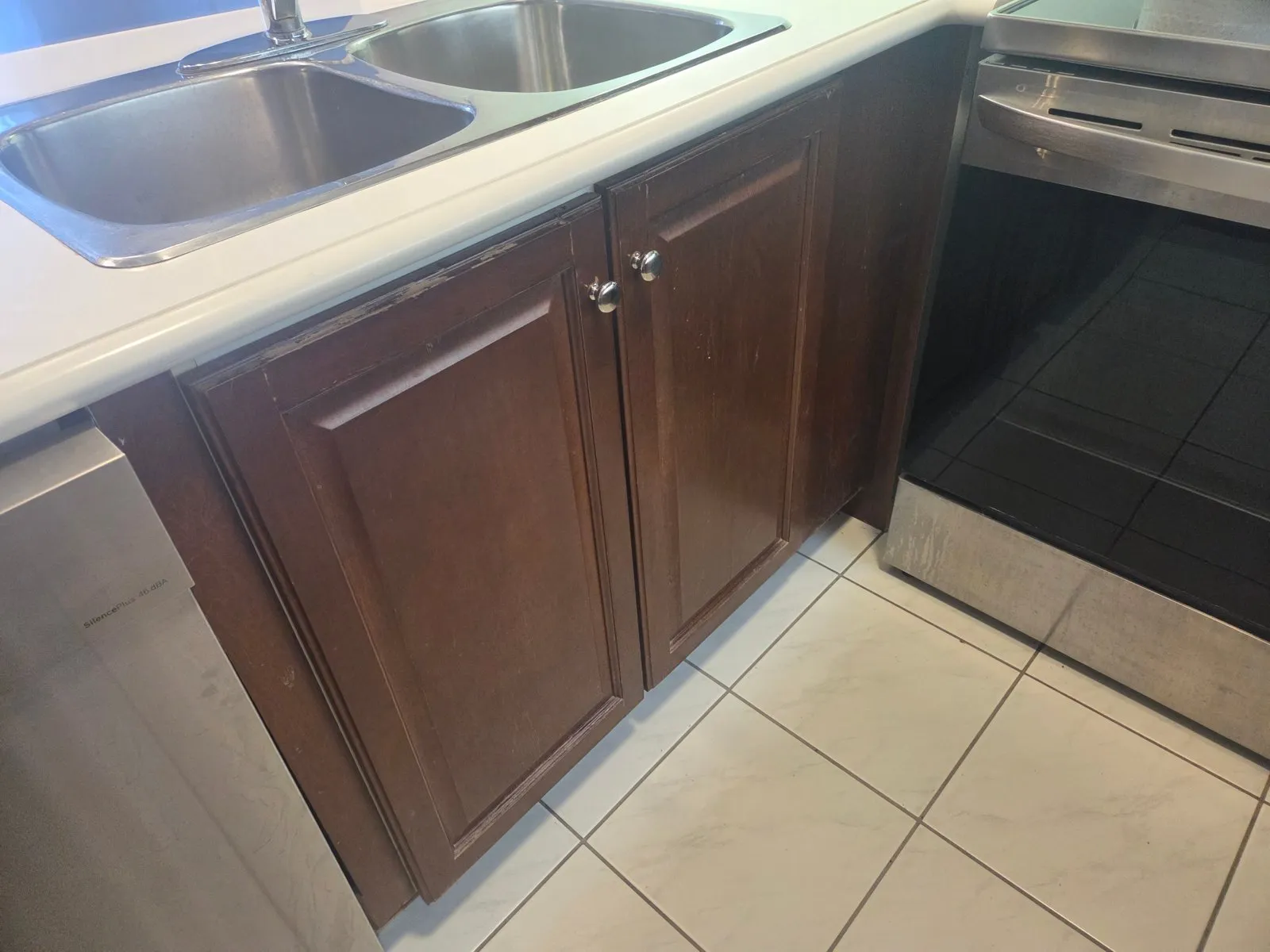 The sink base before the work, cherry doors with round knobs and the finish worn through along the edges
