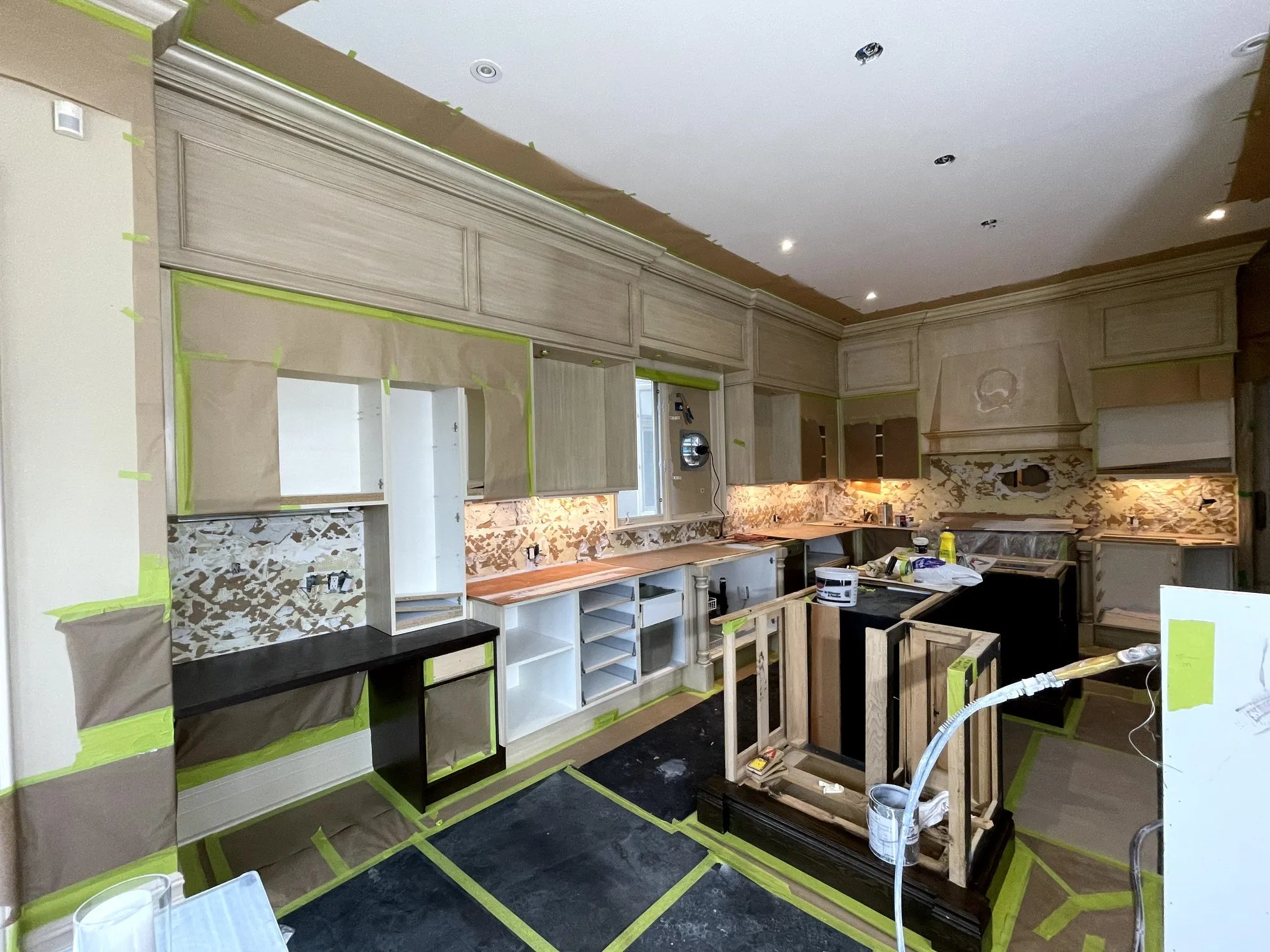 The room under scaffolding with the walls, floor and backsplash masked in plastic and green tape while the crown moulding is worked on