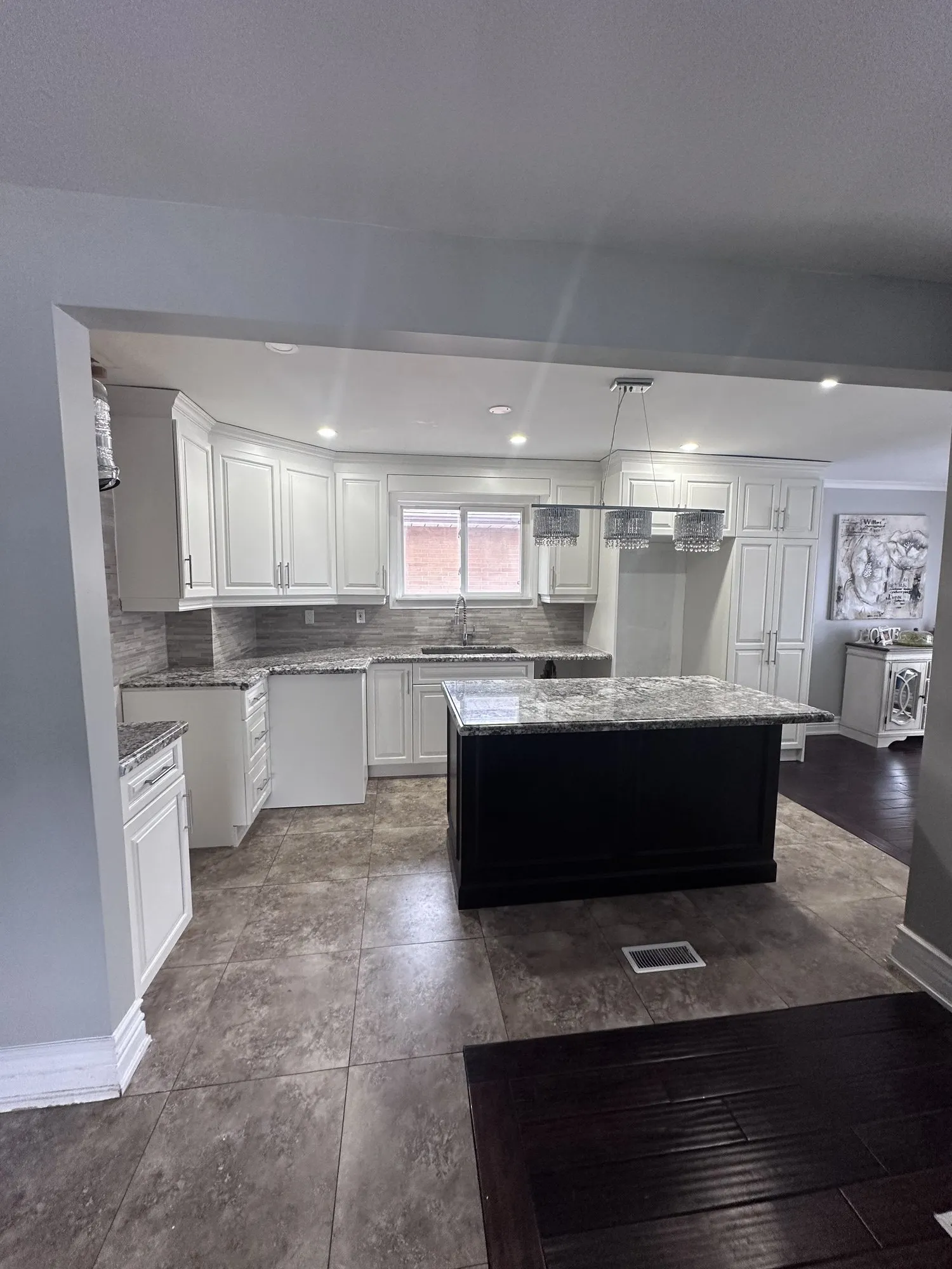 The finished room seen from the hallway, white perimeter cabinetry framing the dark island with the tile floor and granite unchanged