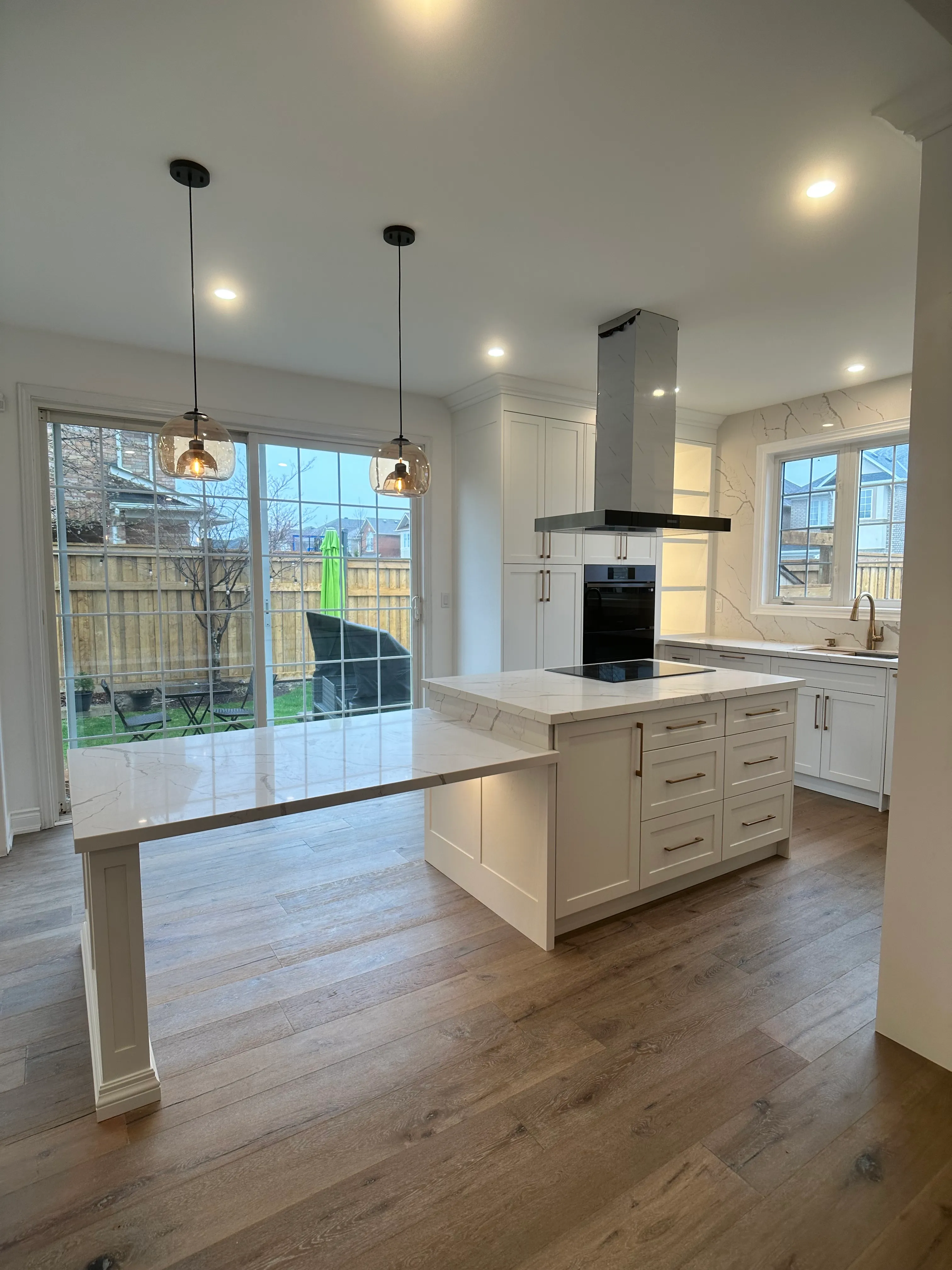 A finished white kitchen with a marble-look waterfall island and full-height slab backsplash, pendant lighting over the island
