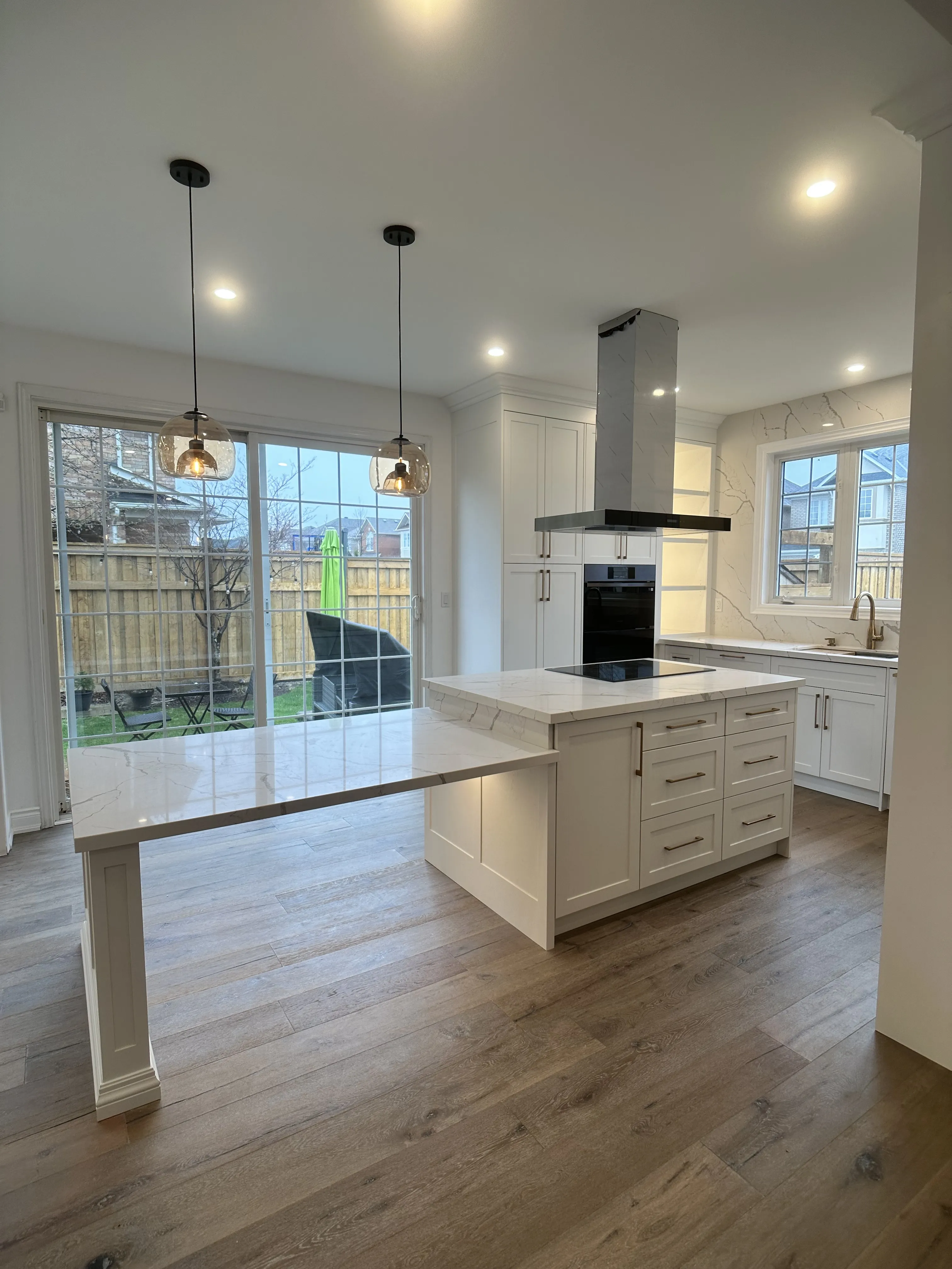 A finished white kitchen with a marble-look waterfall island and full-height slab backsplash, pendant lighting over the island