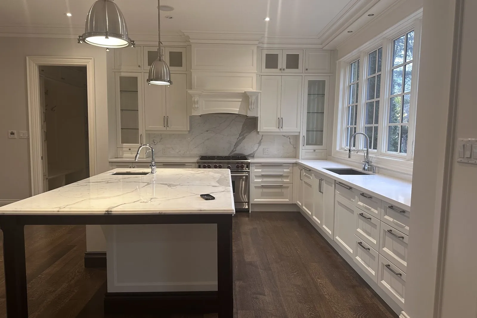 A kitchen island with a veined stone top and a seating overhang, in a finished white kitchen