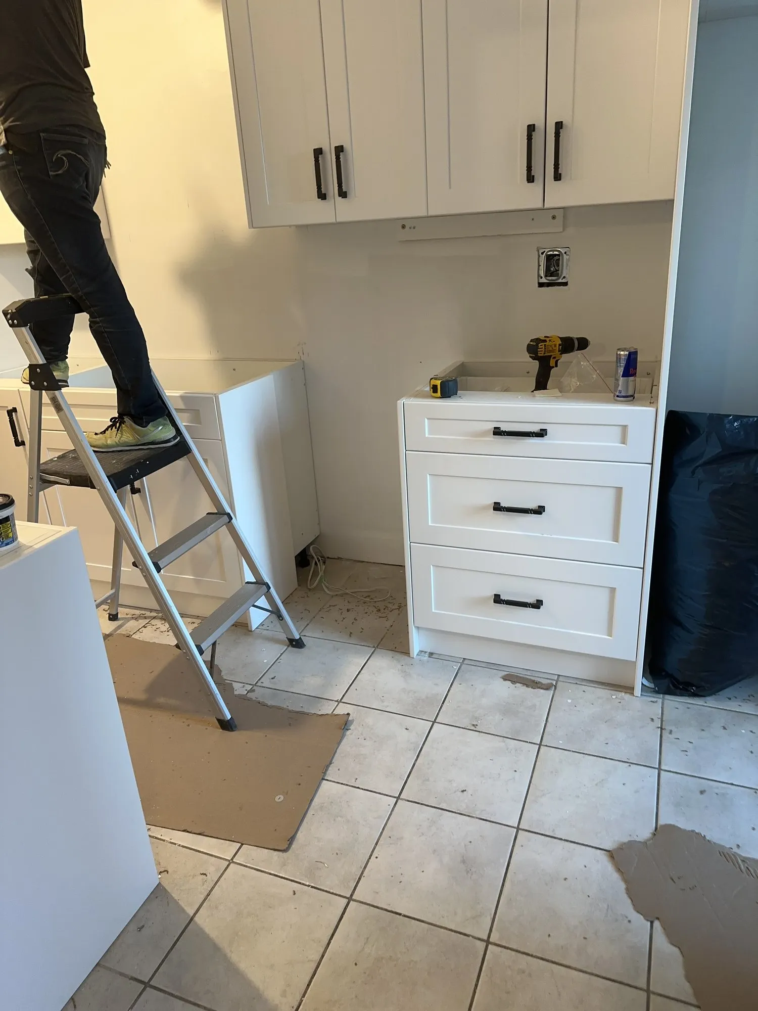 New cabinet carcasses being fitted against a bare wall, one being held in place from a stepladder, with the floor cleared