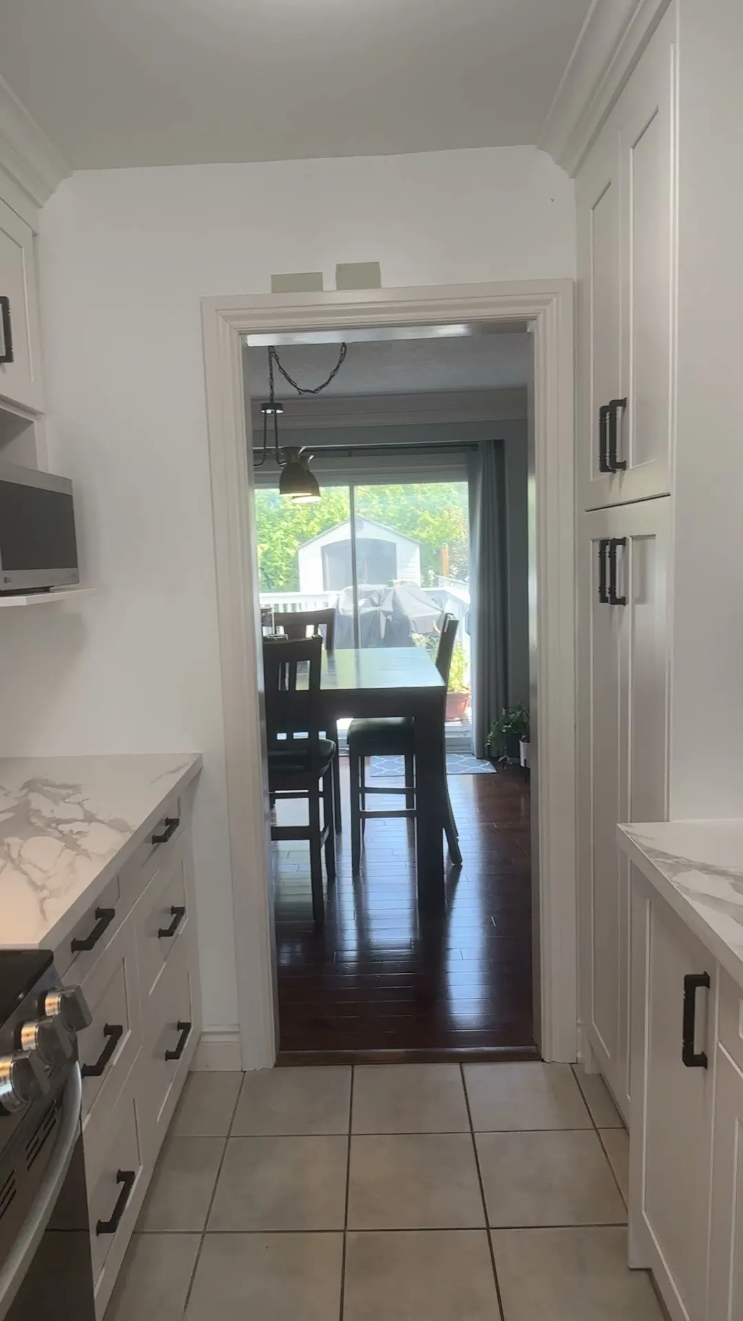 The finished Richview kitchen — a narrow galley in off-white shaker cabinetry with quartz counters, black pulls and floating wood shelves above the sink