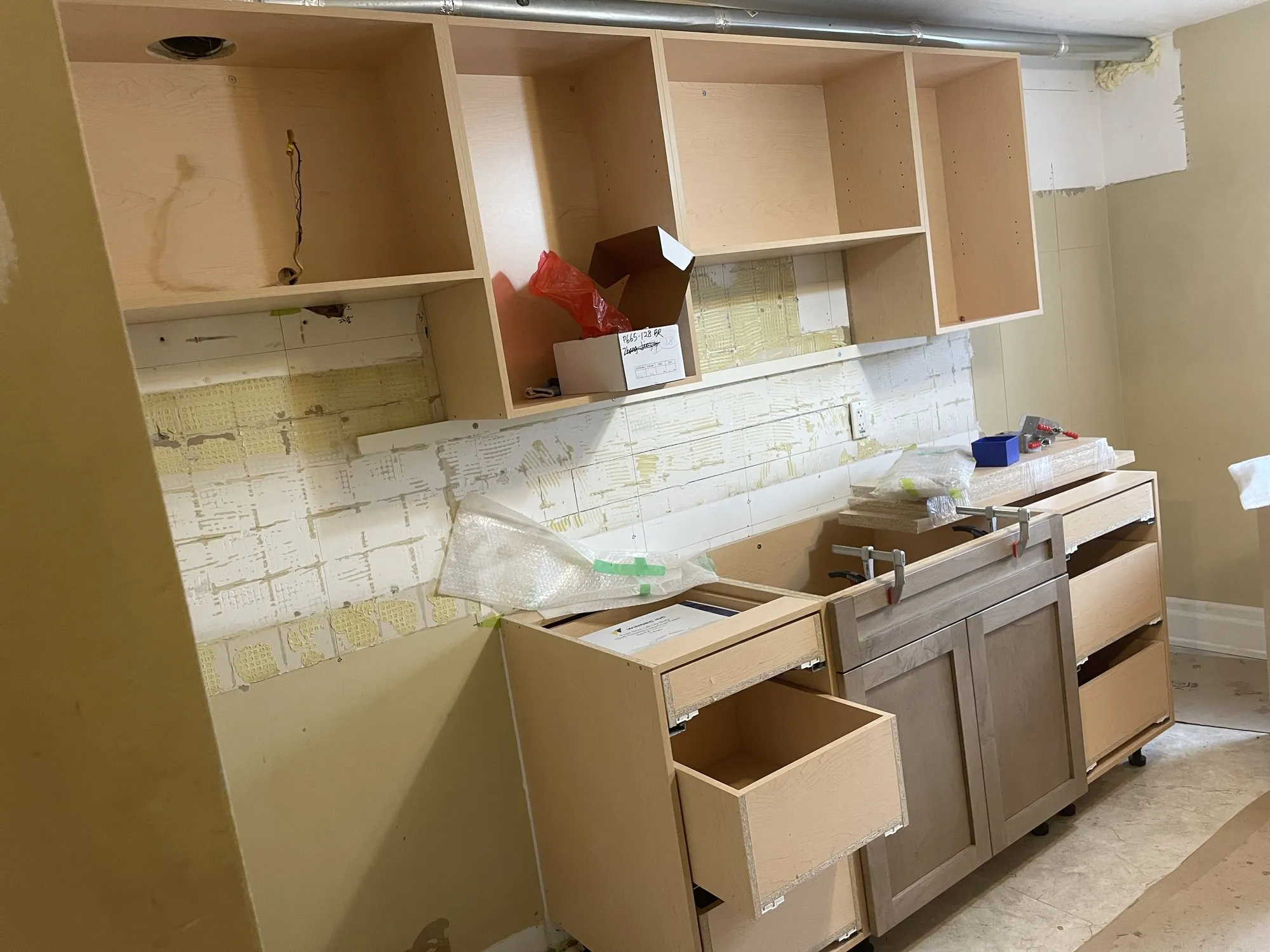 Installation day with the new cabinet boxes standing in place, drawers pulled out and the old tiled backsplash stripped back to the wall