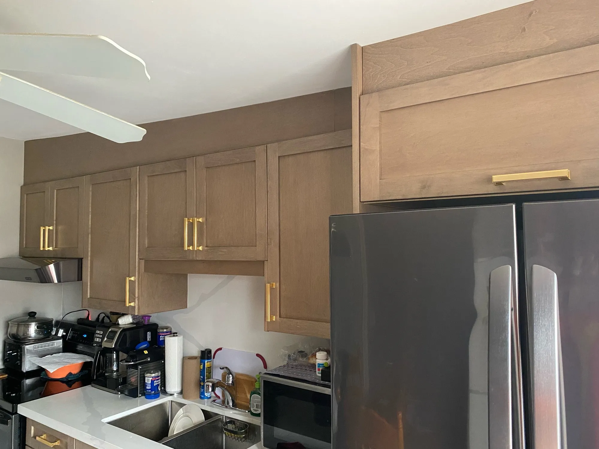 The finished stained cabinets meeting a ceiling that slopes, with a filler panel closing the gap above the tall cabinet beside the fridge