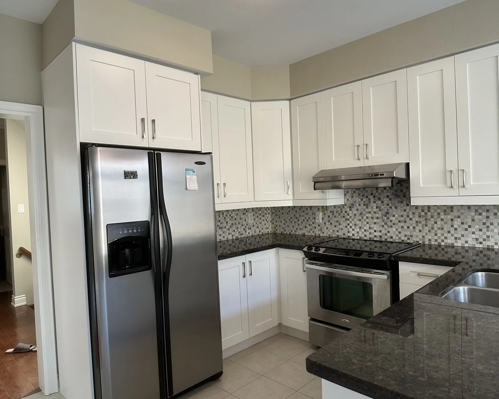 After — A kitchen before and after — dark cherry fronts replaced with white, on the same boxes, with the granite, mosaic backsplash and tile floor all kept