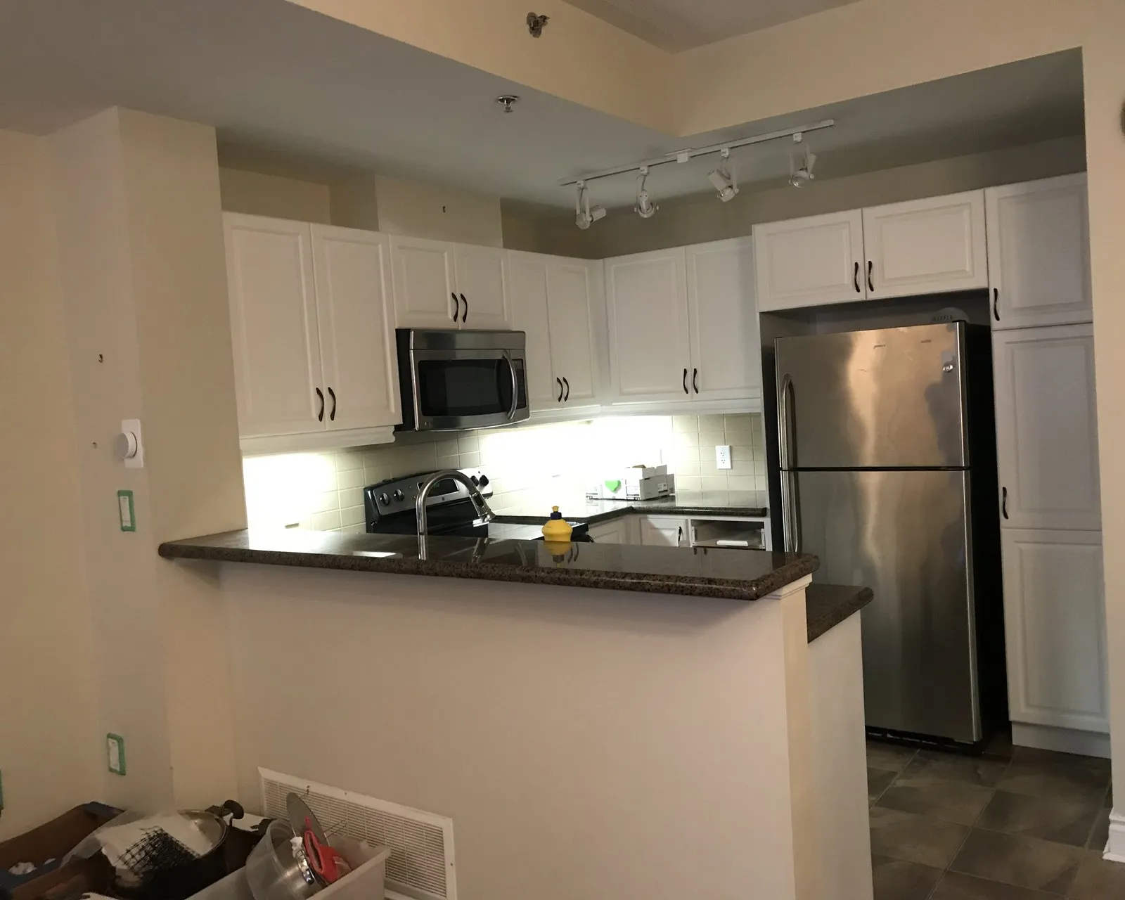 After — A condo galley kitchen before and after refacing — espresso fronts replaced with white on the same boxes, with the granite peninsula and layout unchanged