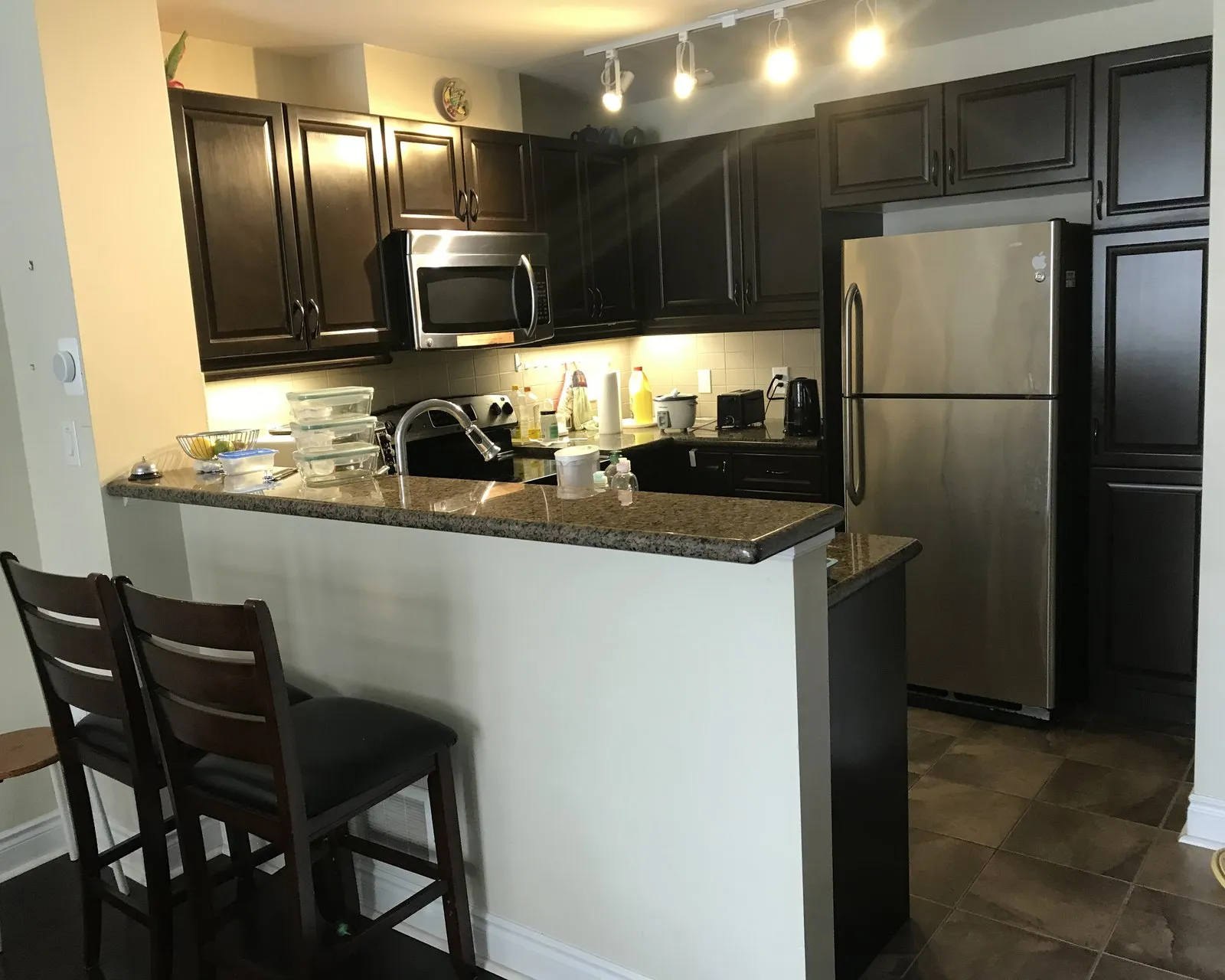 Before — A condo galley kitchen before and after refacing — espresso fronts replaced with white on the same boxes, with the granite peninsula and layout unchanged