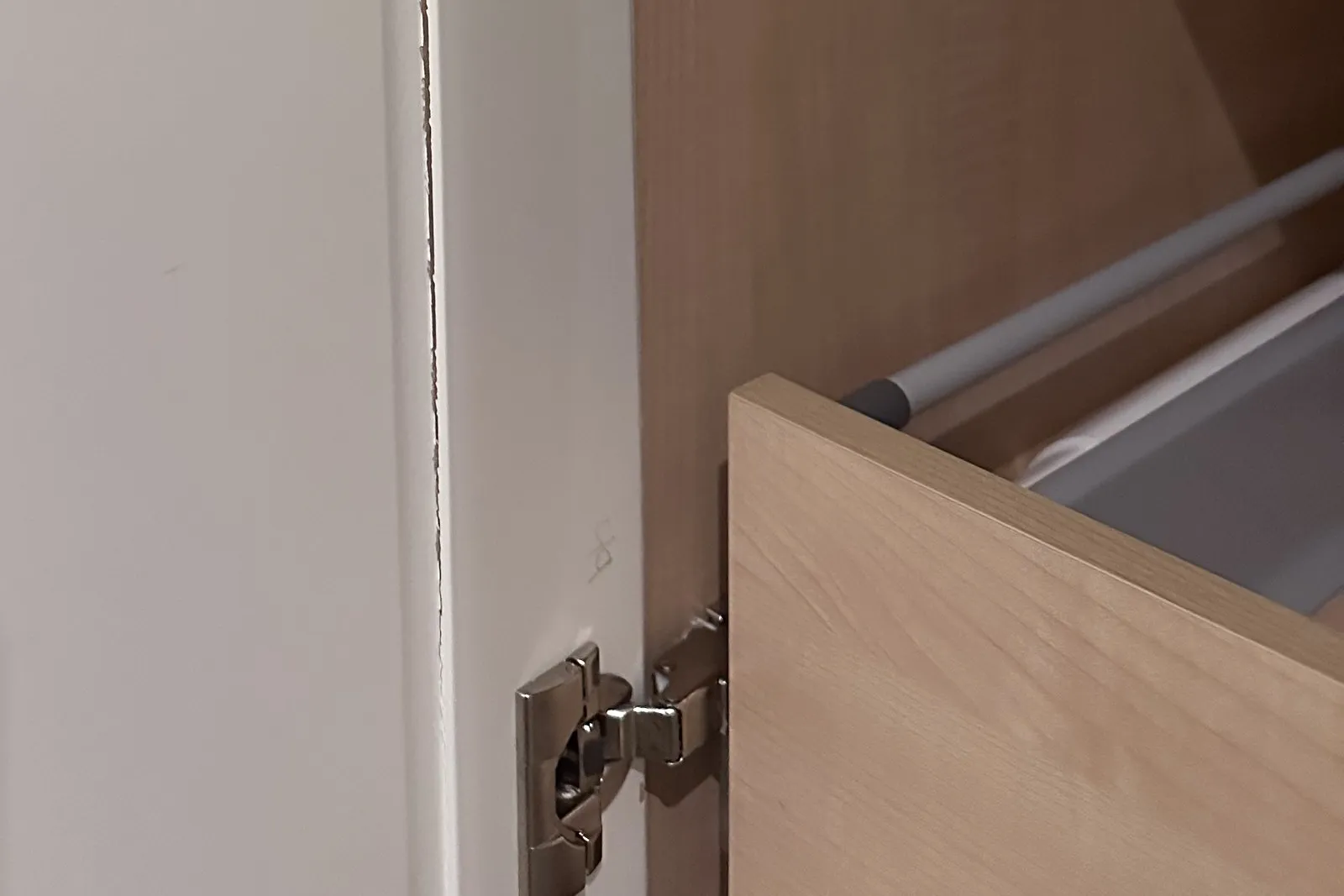 A concealed soft-close hinge on a cabinet door, beside a birch drawer box running on an undermount runner