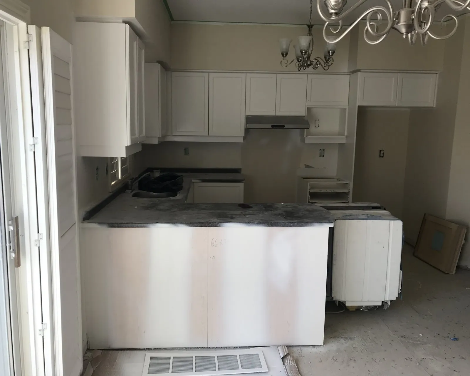 A kitchen sealed for spraying — base cabinets and island sheeted in plastic, the wall cabinets masked, with the doors already away at the shop