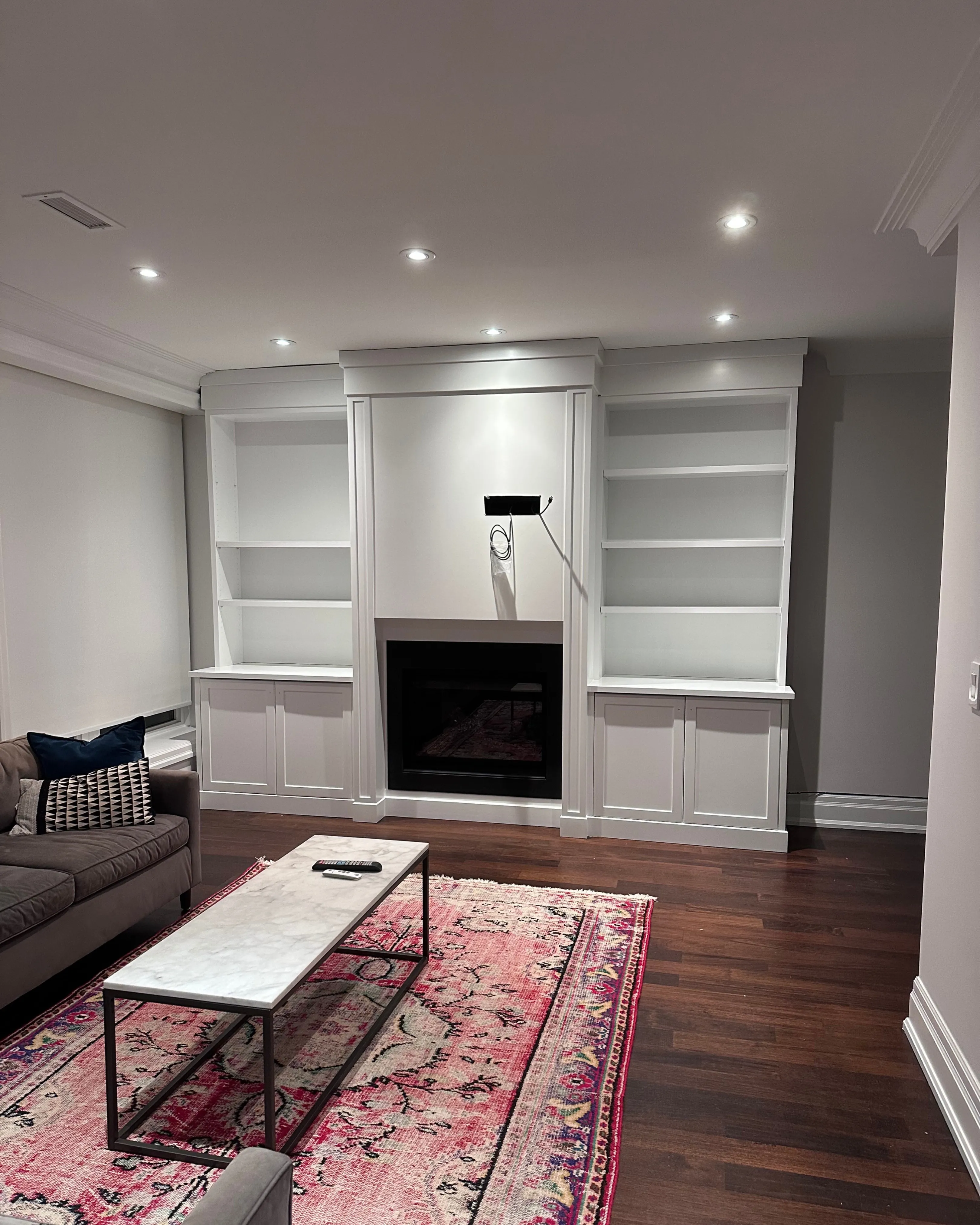 After — A built-in shelving unit around a fireplace, before in dark espresso wood and after painted crisp white, the same room and the same angle