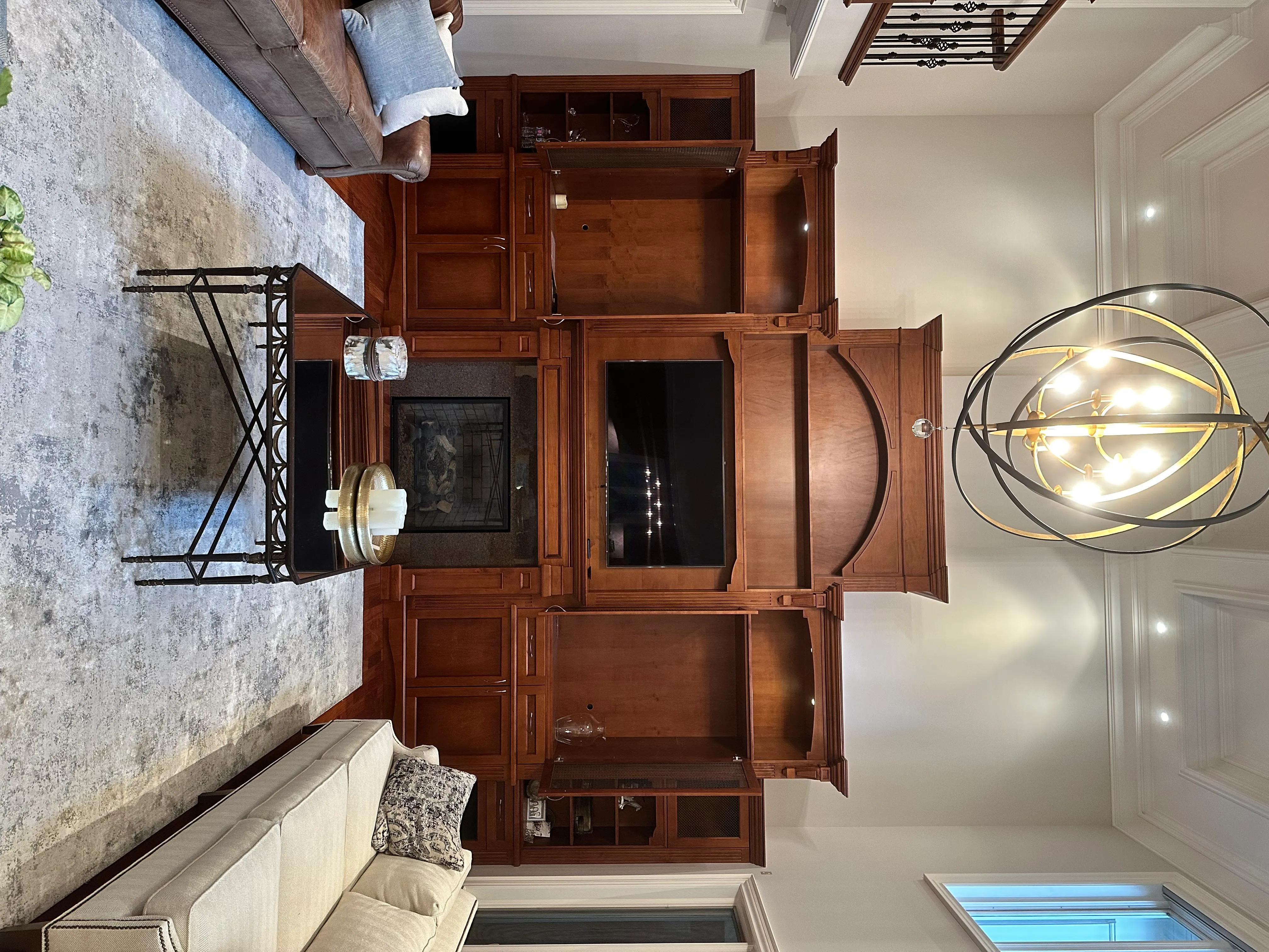 An ornate stained wood entertainment built-in around a fireplace, the arched pediment and crown detail reading clearly through a warm cherry stain