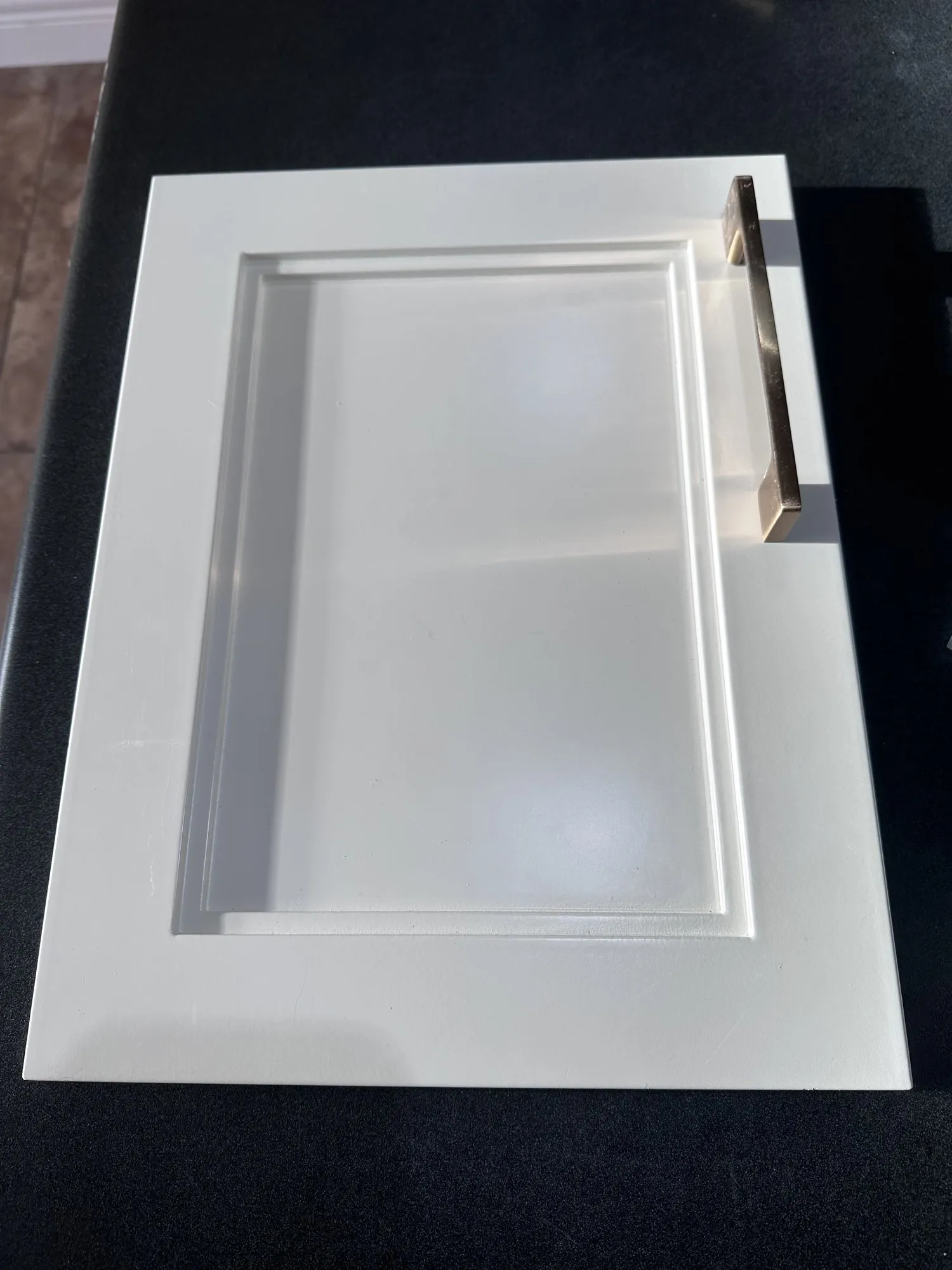 A single finished door lying face up on black felt in the shop, showing the arched raised-panel profile sprayed white