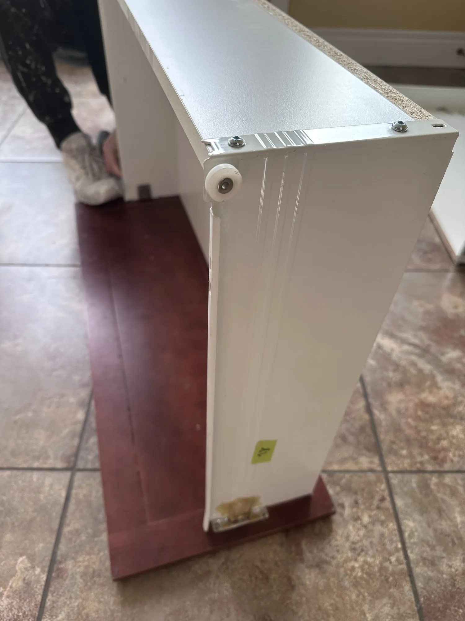 A finished white end panel being carried back into the kitchen and held up beside an original dark cherry panel that has not been done yet