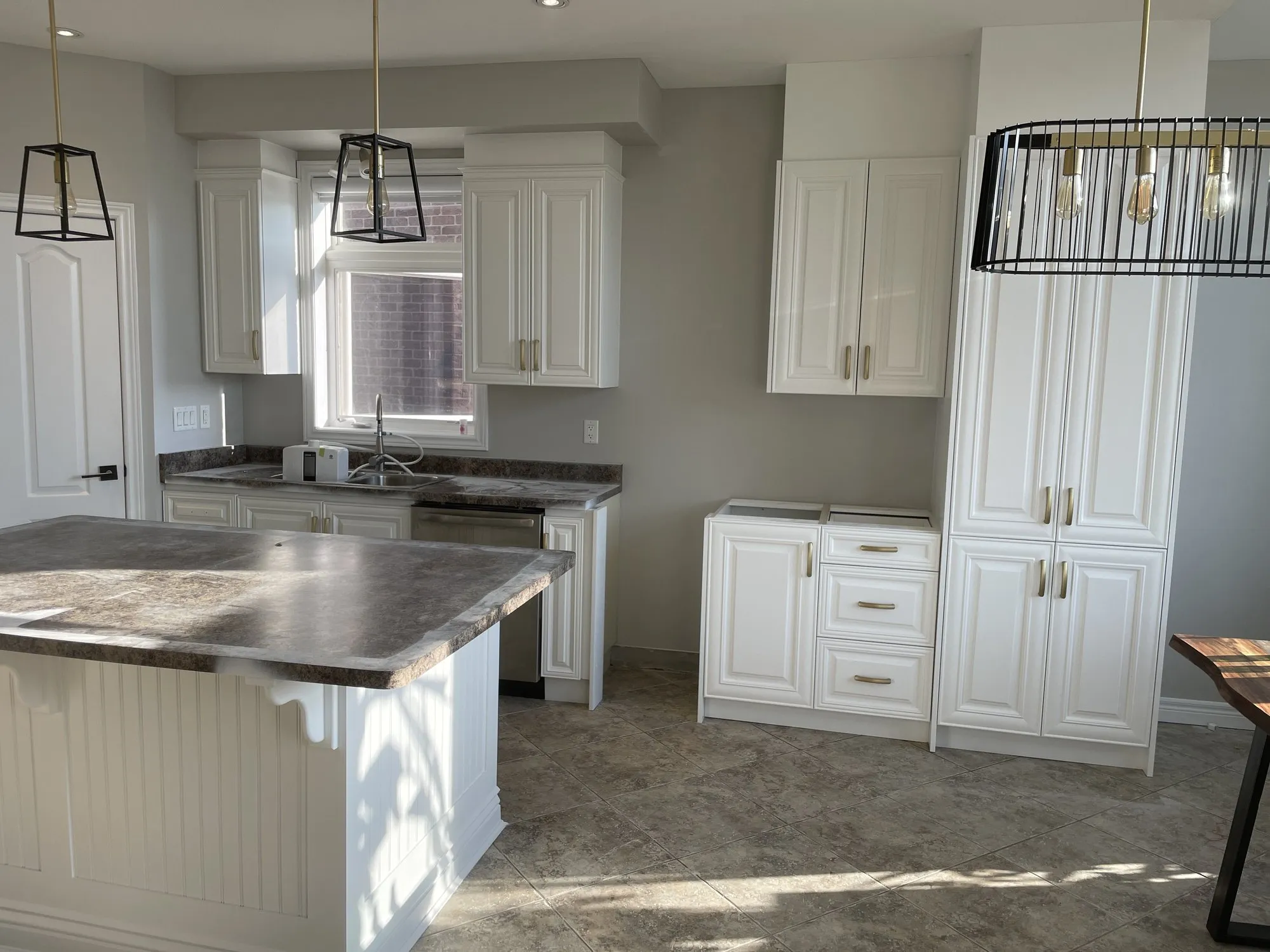The finished white island and tall cabinet run, with the original speckled laminate counters and tiled floor unchanged