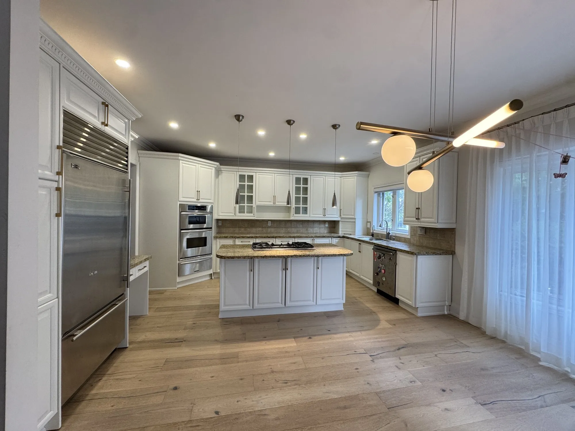 The finished kitchen in Cloud White with the island, wall ovens and original granite counters and wood floor