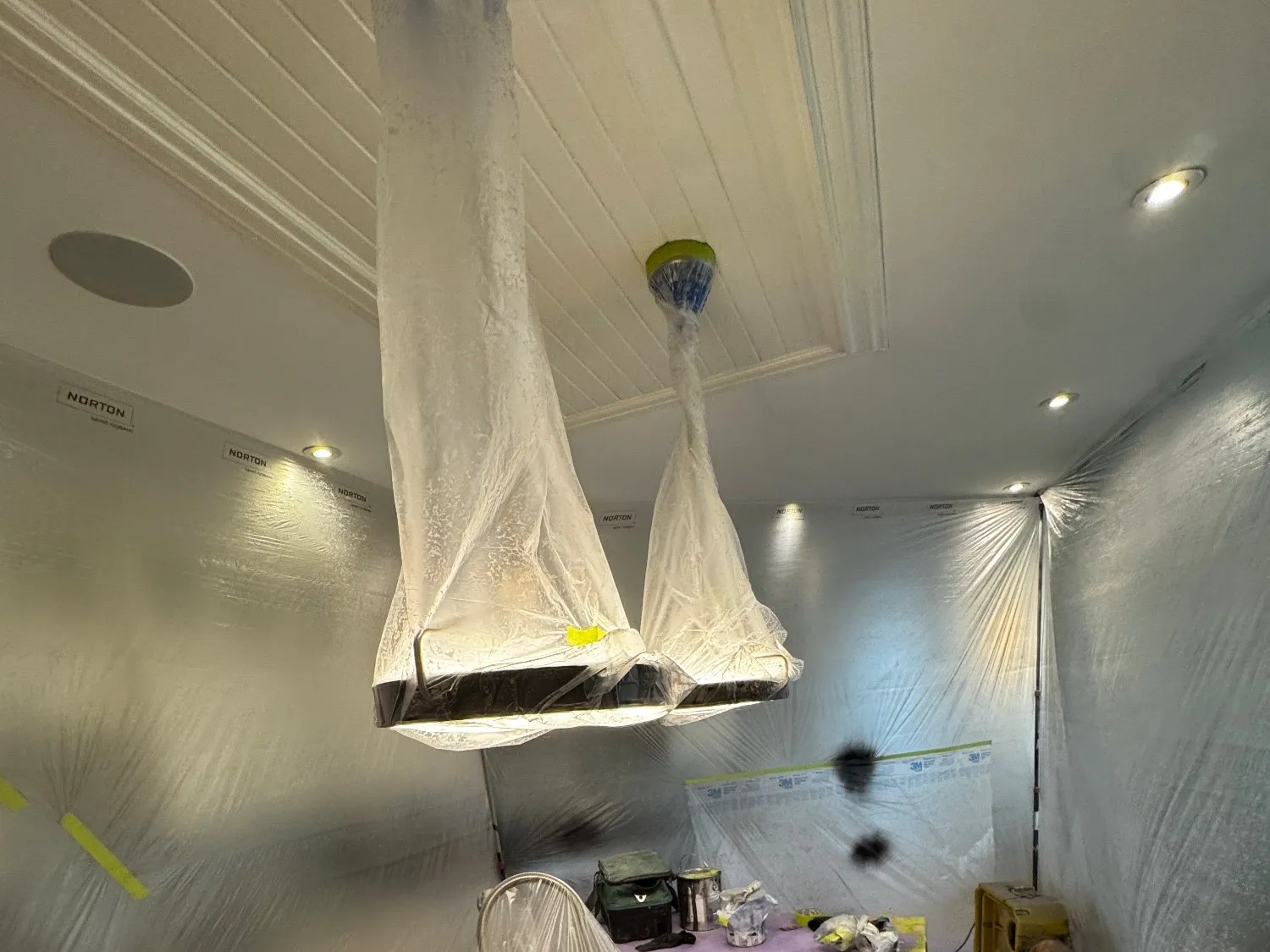 The kitchen sealed behind plastic sheeting with the pendant lights bagged and the floor covered, before anything is sprayed