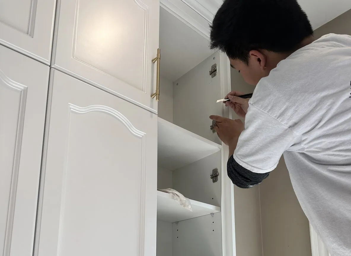 A crew member marks a hinge position inside a painted upper cabinet before its door goes back on