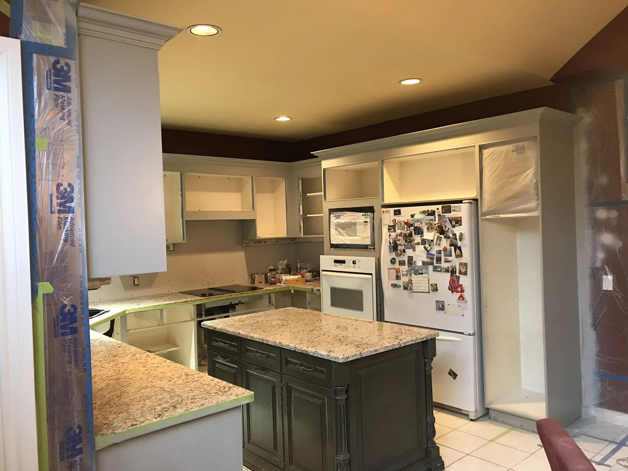 Cabinet boxes sprayed in place with the doors off, counters and appliances masked behind 3M film