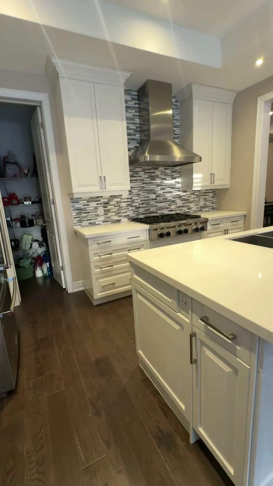 The finished Glenorchy kitchen — dark espresso cabinetry sprayed white around a large island, with the white quartz counters, mosaic backsplash and hardwood floor unchanged