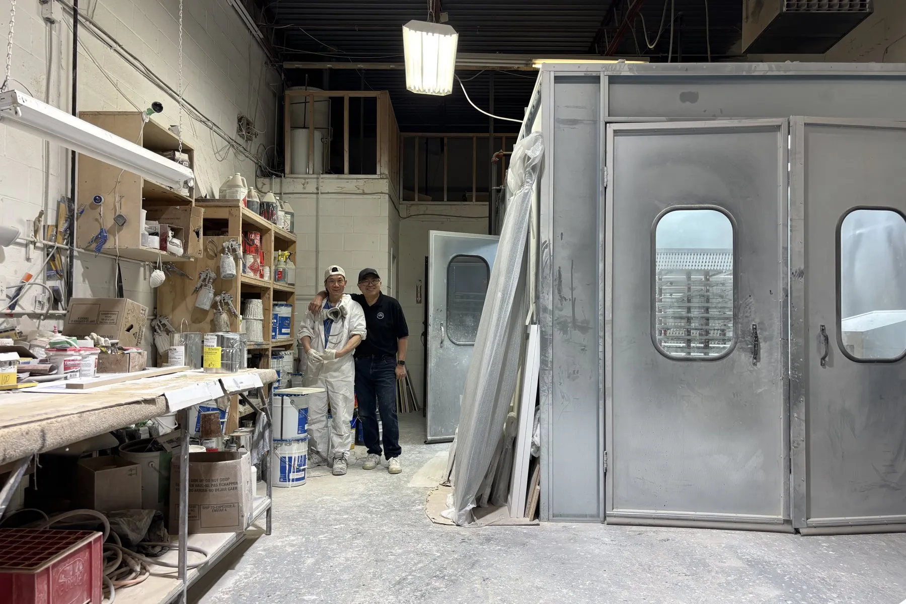The Kitchen Made New spray booth in Oakville, with two of the crew beside it — where the doors and drawer fronts are finished