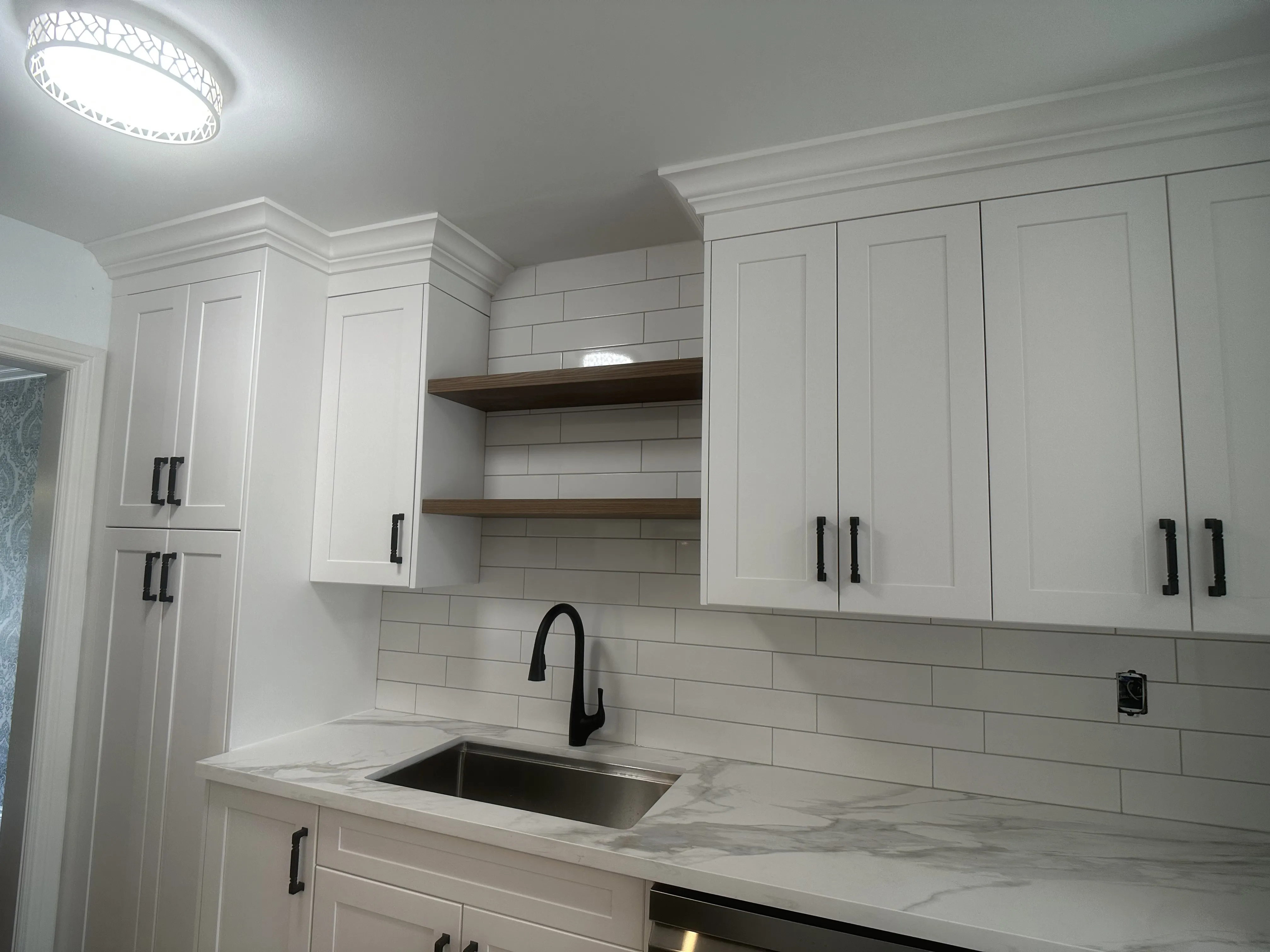 A quartz counter with soft grey veining at a sink and black faucet, white subway tile backsplash behind it