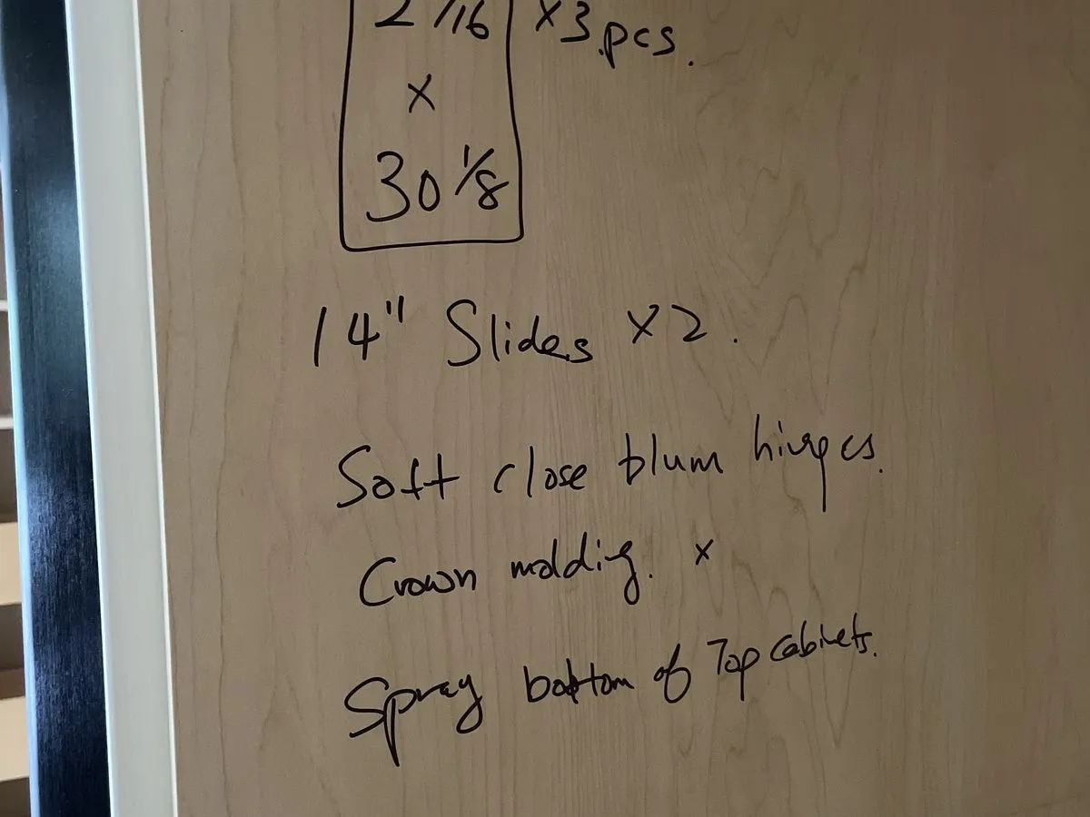 A job spec handwritten on plywood — slide sizes, "Soft close Blum hinges," crown moulding, noted as a real line on a real order