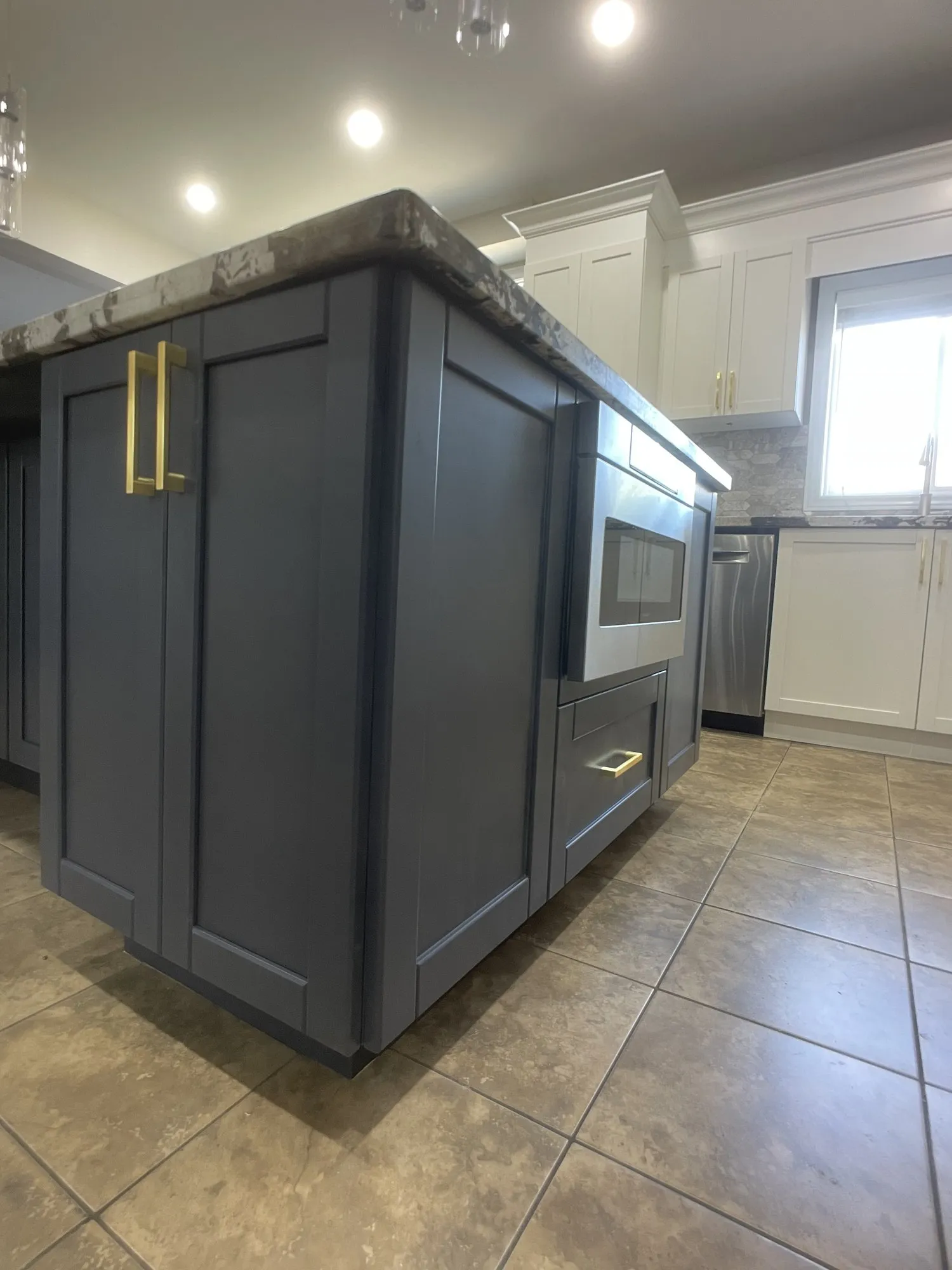 The finished charcoal island with brass handles and glass-fronted doors, under the original speckled granite