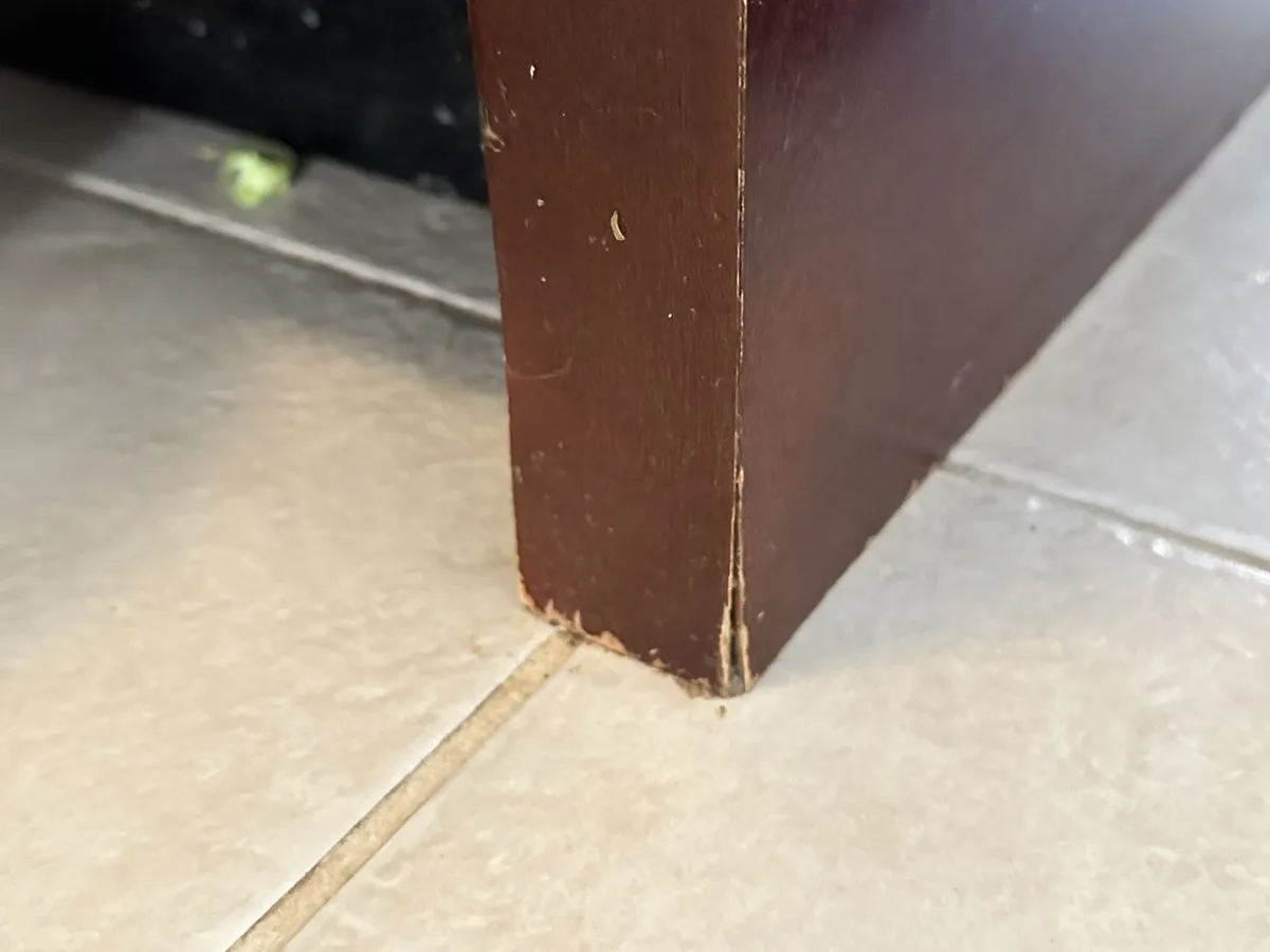 A cabinet panel's laminate face lifting and peeling away from swollen board at a base corner